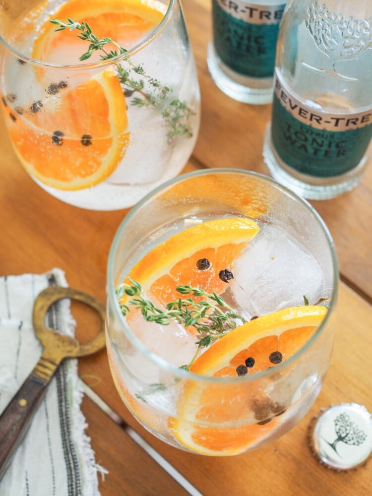 Gin and tonics garnished with orange slices, thyme, and peppercorns.