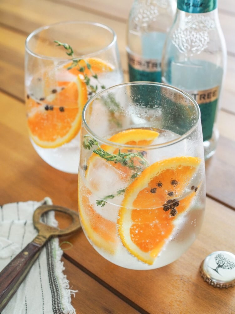 Two gin and tonics garnished with orange slices, thyme, and peppercorns. 