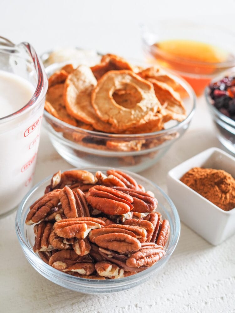 Sunny side shot of microwave oatmeal toppings including pecans, milk, apple slices, honey, and cinnamon.