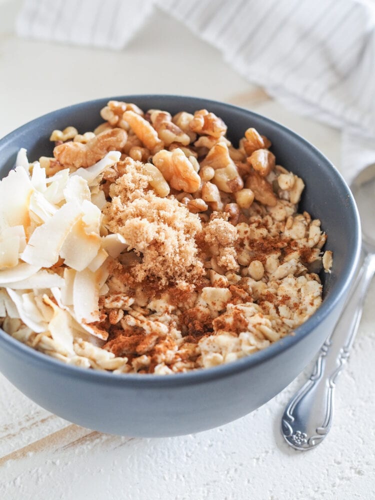 Bowl of microwave oatmeal in a blue bowl on a white table. Toppings include toasted coconut, brown sugar, and walnuts.