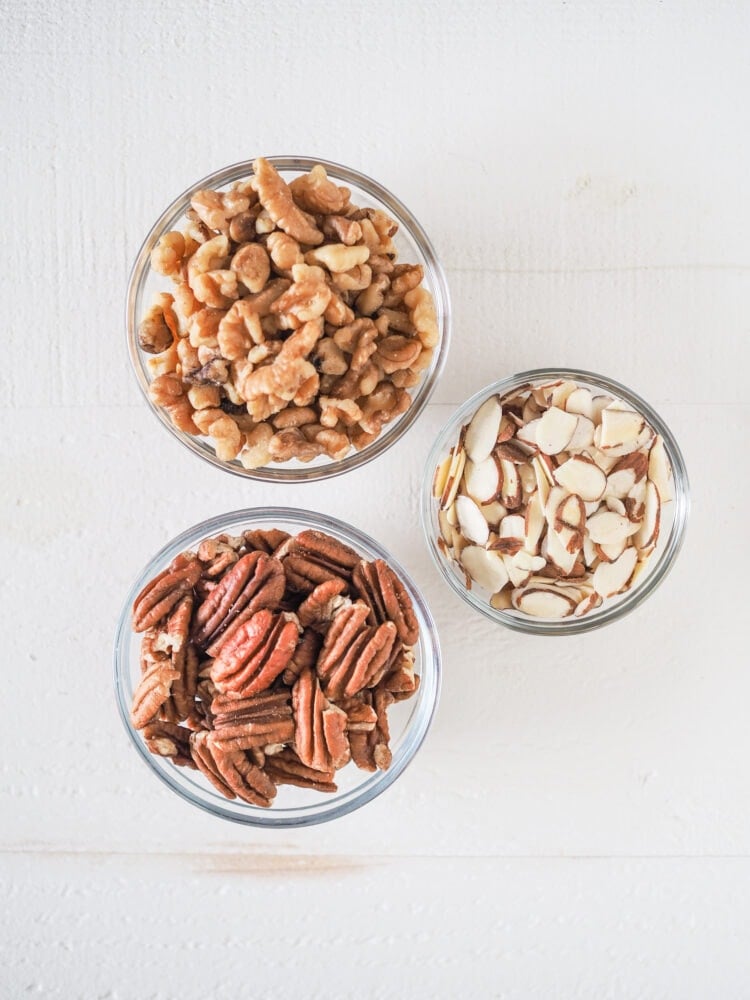 Overhead shot of nuts in prep bowls: walnuts, pecans, sliced almonds.