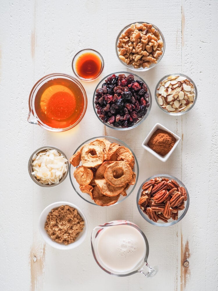 Overhead shot of microwave oatmeal toppings in prep bowls including: vanilla, honey, dried berries, walnuts, almond slices, shaved coconut, dried apples, cinnamon, pecans, brown sugar, and milk.