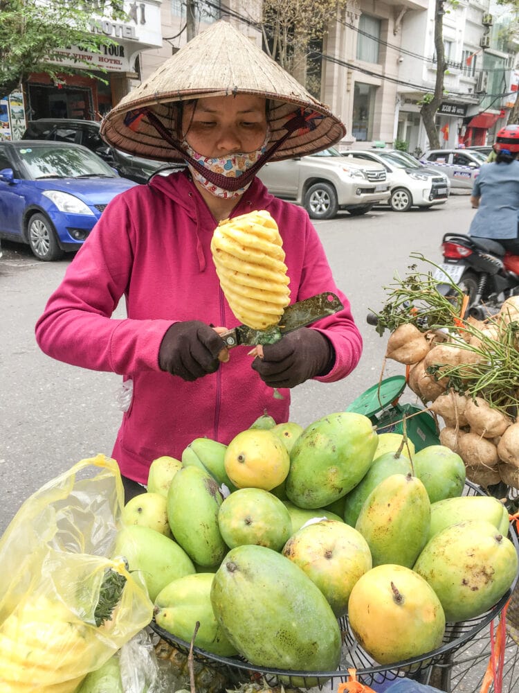 Woman wearing conical hat carving mango on the streets of Hanoi.