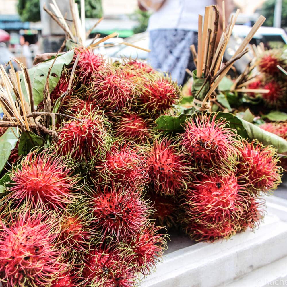 Bouquets of hot pink spiky rambutan fruit tied together and stacked at a market in Myanmar.