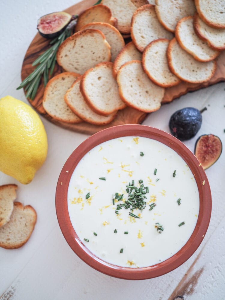 Overhead shot of whipped ricotta dip tipped with lemon zest, chopped fresh rosemary, and a wood board with crackers and figs. 