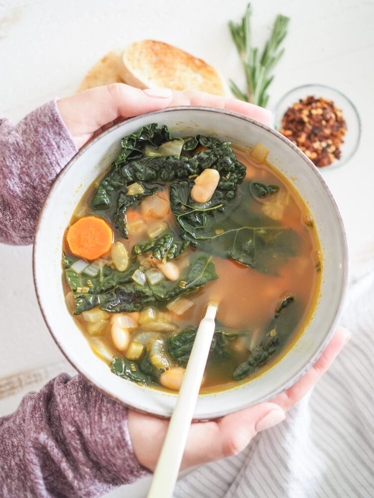 Hands holding a bowl of white bean soup.