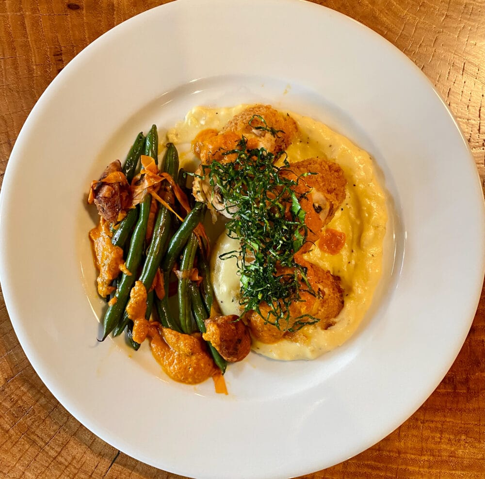 Overhead shot of a dish from Church Hill Variety: Sou vide stuffed chicken roulade, panko crusted and fried on a bed of mashed yukon gold potatoes and topped with fried julienne cut collard greens. Served with a side of green beans.