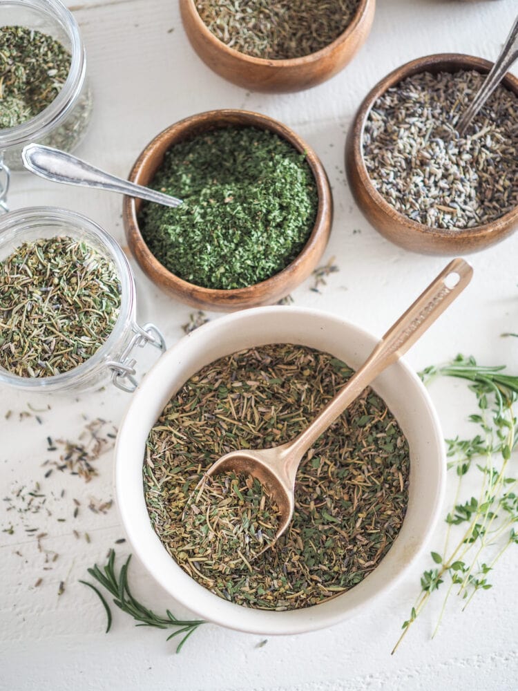 Blending herbs de Provence in a large bowl, with individual smaller bowls of spices surrounding it.