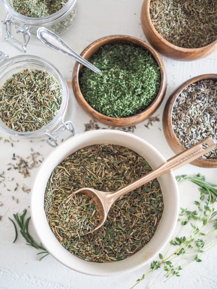 Overhead shot of multiple bowls of spices to blend into the larger bowl of herbs de Provence.