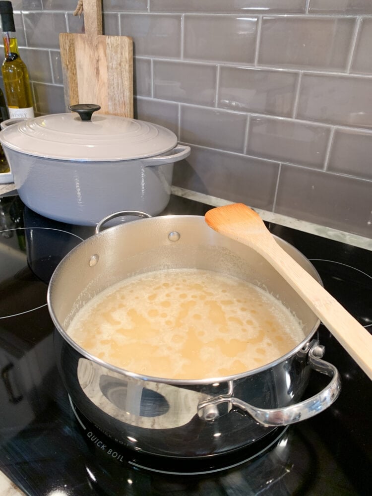 A large stainless steel cooking pot with cornmeal and boiling water in the process of cooking.