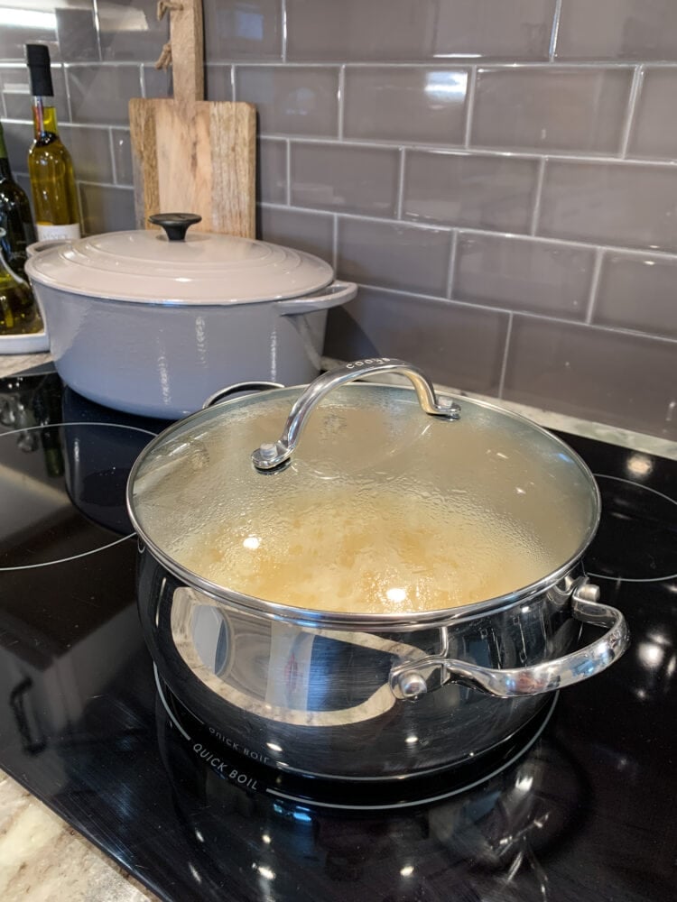 Photo of a large stainless steel pot filled with cooking grits on a stovetop.