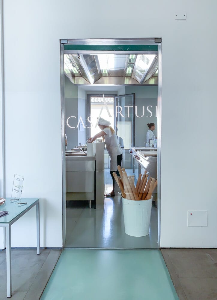 Glass entrance to the Casa Artusi cooking school with a bucket of pasta rolling pins and instructors working in the back.