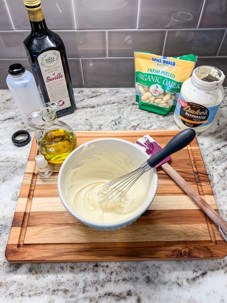 Making aioli, a bowl of mayonnaise and olive oil whisked together with garlic and squeeze bottle for serving in the background.