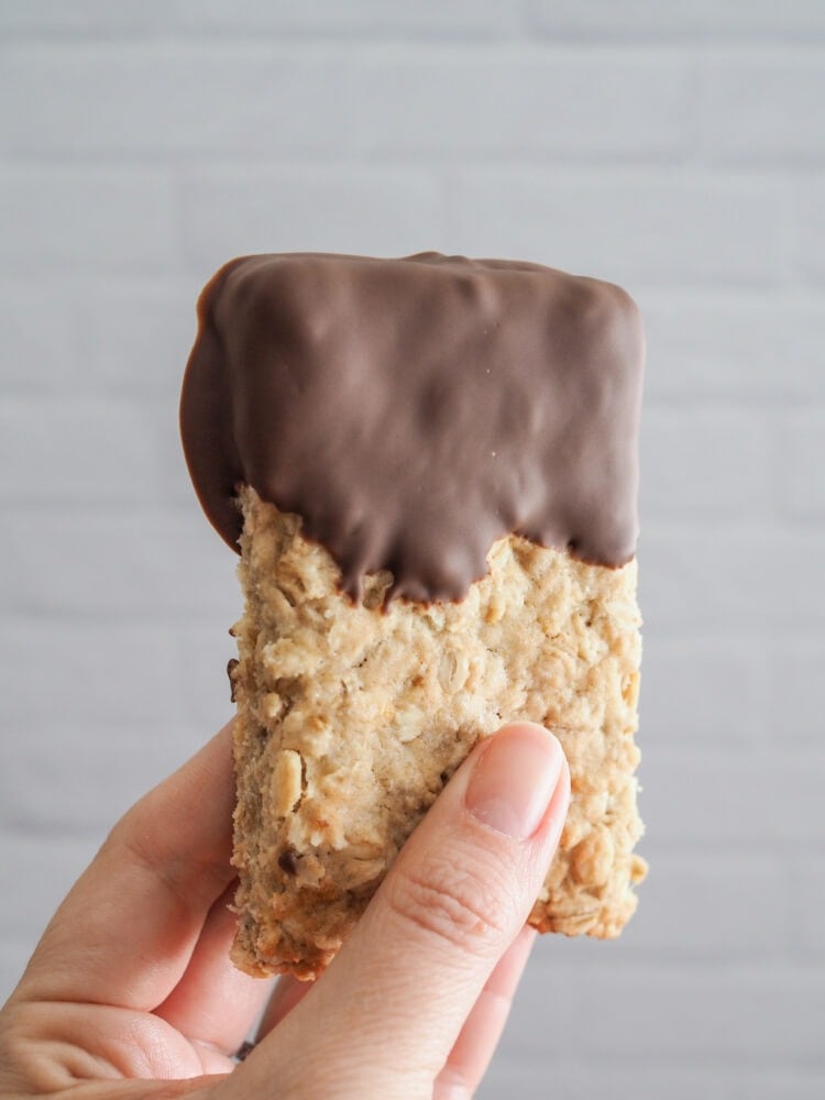 A hand holding up a plain oatcake dipped in chocolate.