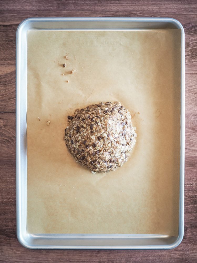 Chocolate chip oatcakes dough formed into a ball and centered on a parchment paper lined cookie sheet.