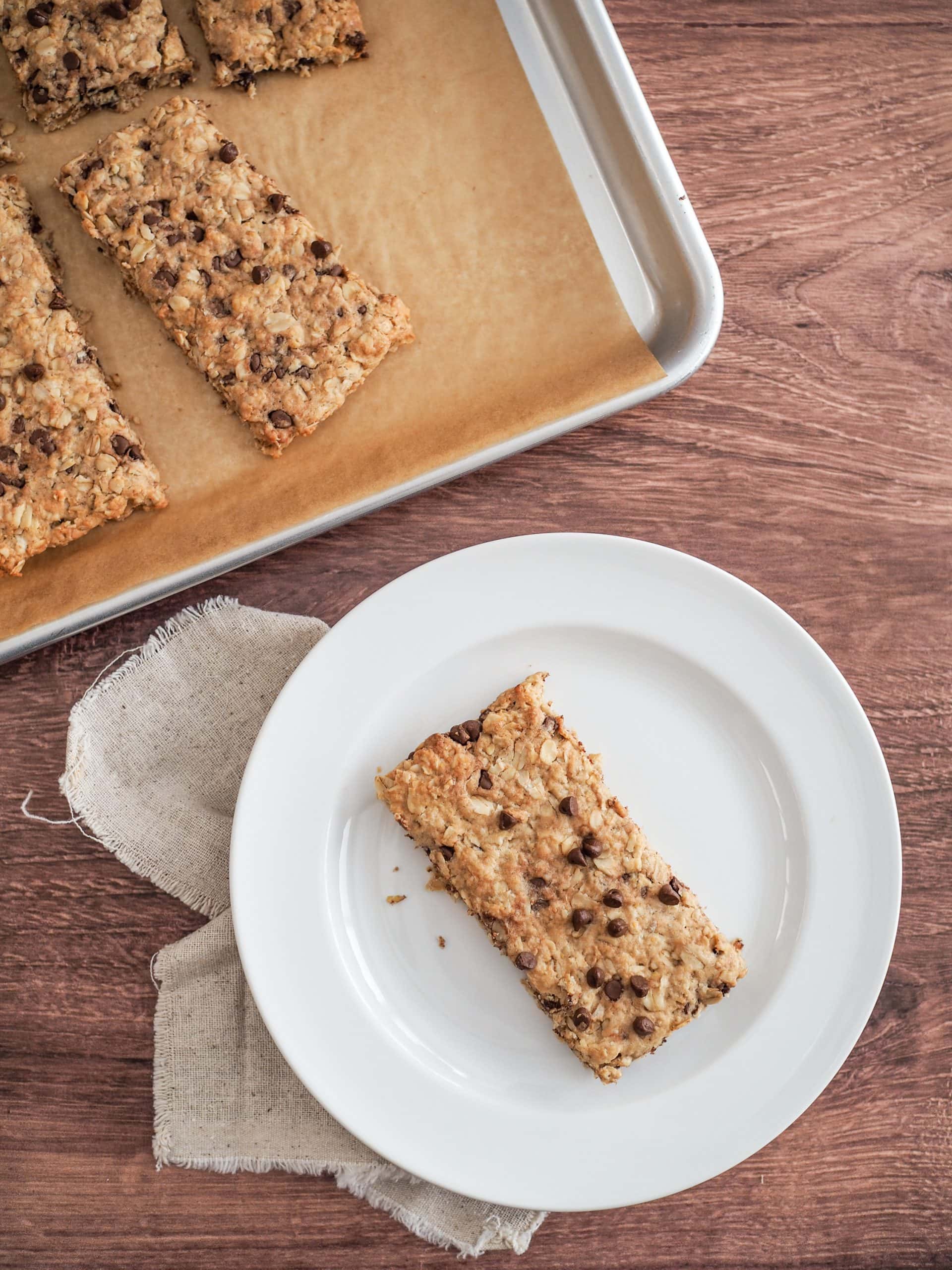 Overhead look at a sheet pan of baked chocolate chip oatcakes with one on a white plate.