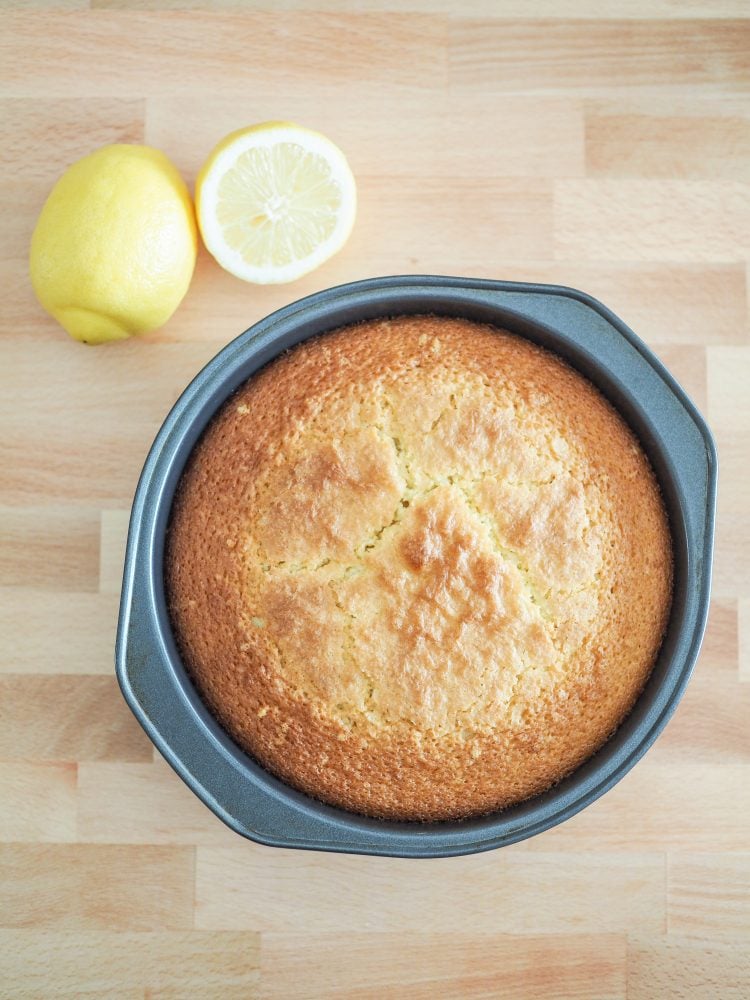 Overhead shot of the finished baked cake in a cake pan with lemons on the side for decoration.