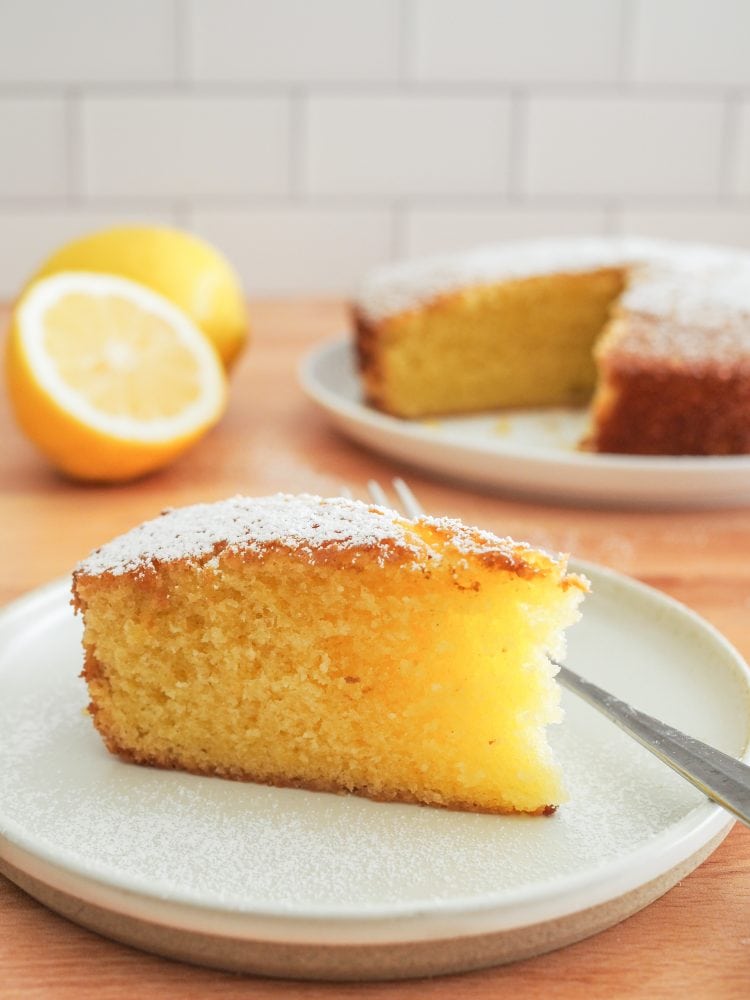 A slice of lemon olive oil cake sprinkled with powdered sugar showing the bright yellow lemon color and dense fluffy texture.