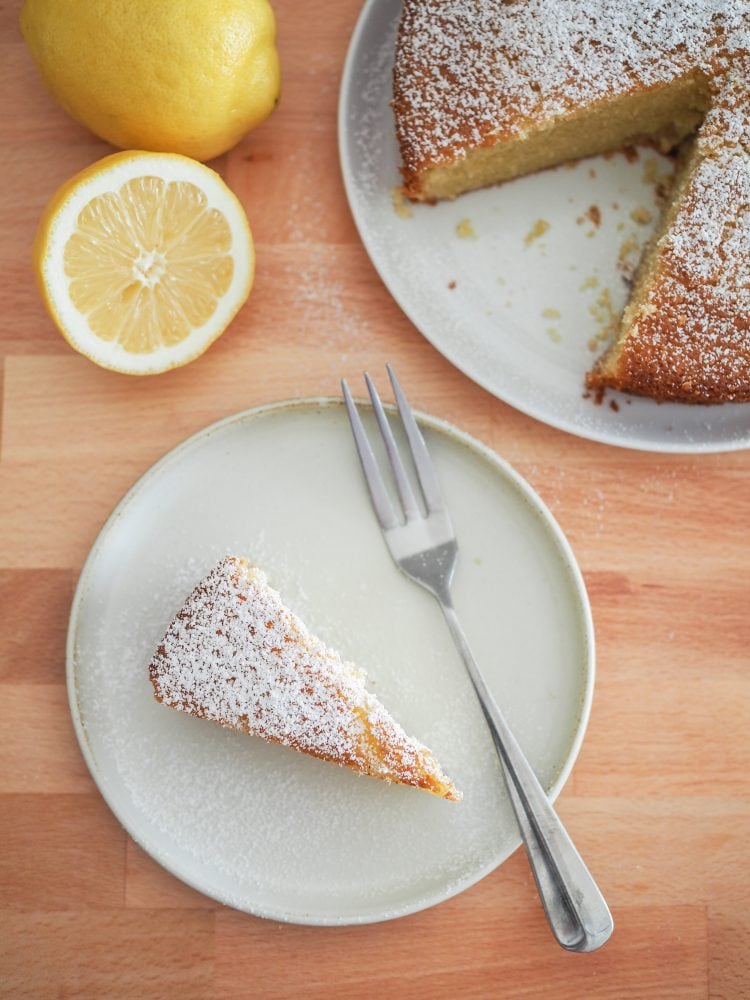 Overhead shot of a slice of lemon olive oil cake sprinkled with powdered sugar and the whole cake to the side.
