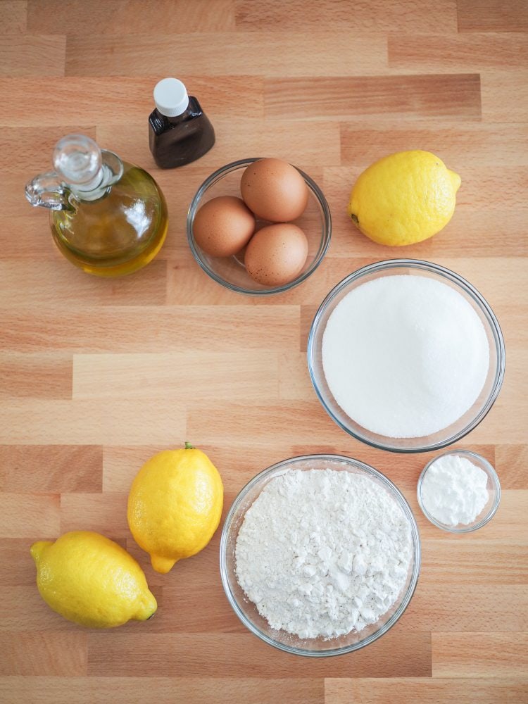 Overhead shot of ingredients for lemon olive oil cake including lemons, olive oil, lemon extract, eggs, sugar, flour, baking powder.