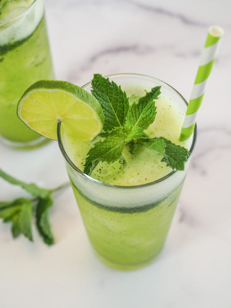 A glass of mint lemonade with slice of lime and sprig of mint as garnish, and a green and white paper straw.