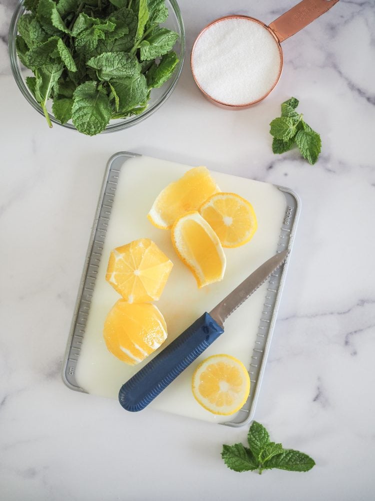 Overhead shot of knife and cutting board with whole lemons showing peels removed with knife.