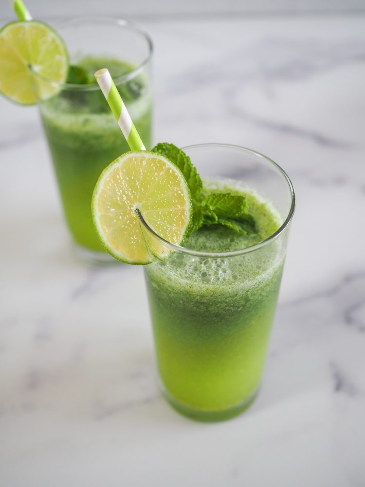 A glass of mint lemonade with slice of lime and sprig of mint as garnish, and a green and white paper straw.