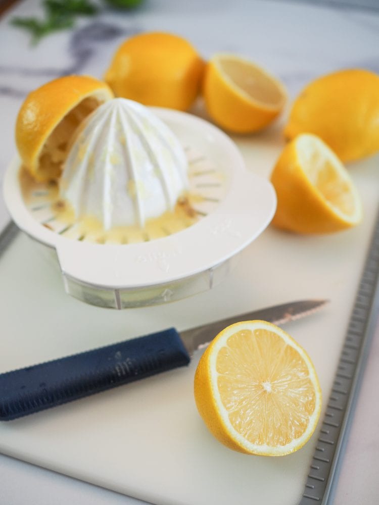 Photo of knife and cutting board with fresh lemons cut in half and a hand juicer.