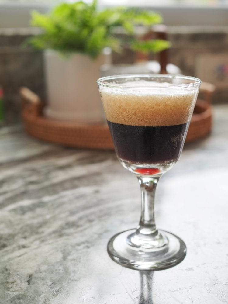 Side view of a shakerato (Italian iced coffee) in a clear glass showing foamy crema on top.