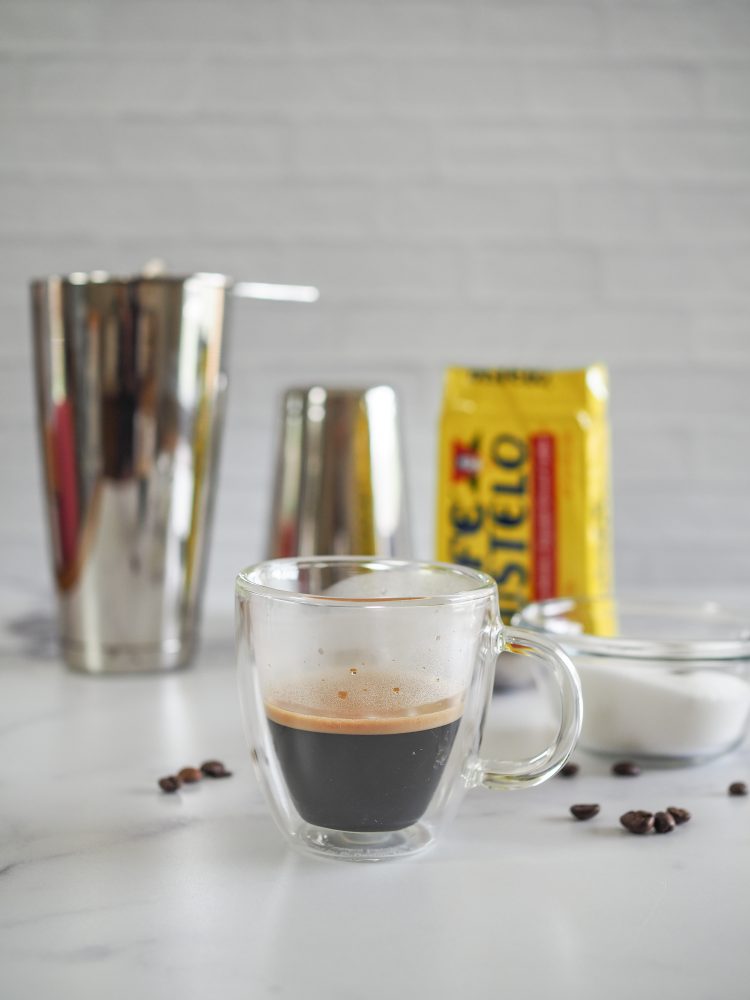 Freshly brewed espresso with cafe bustelo, sugar, and martini shaker in background.