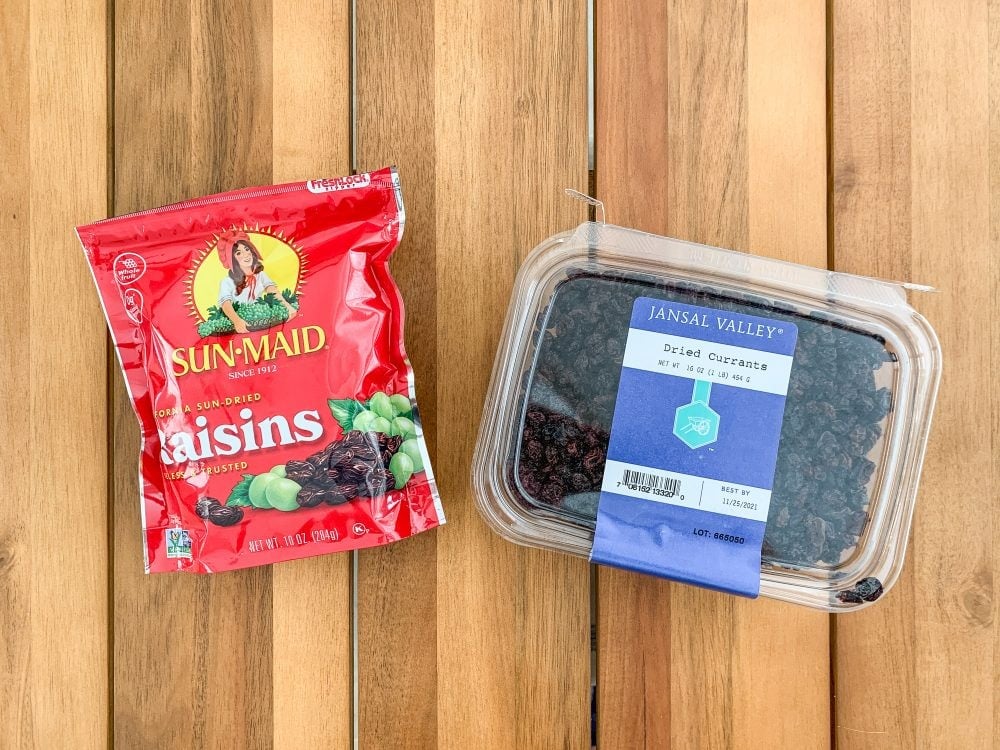 A bag of raisins and a clear plastic box of currants. 