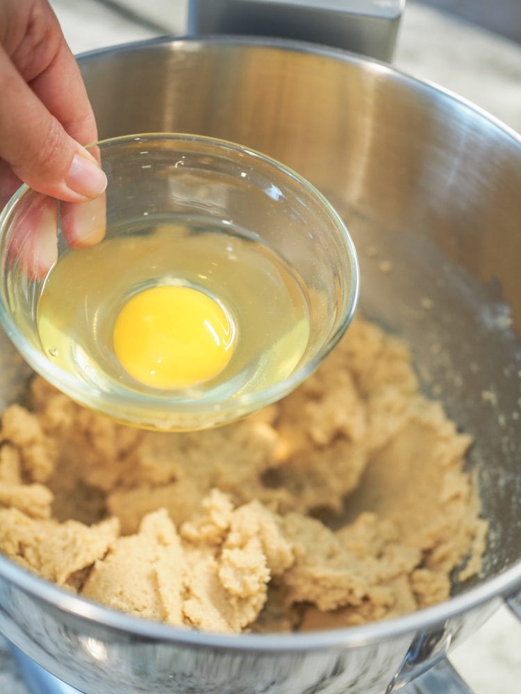 Look inside stand mixer bowl showing an egg being added to cookie dough.