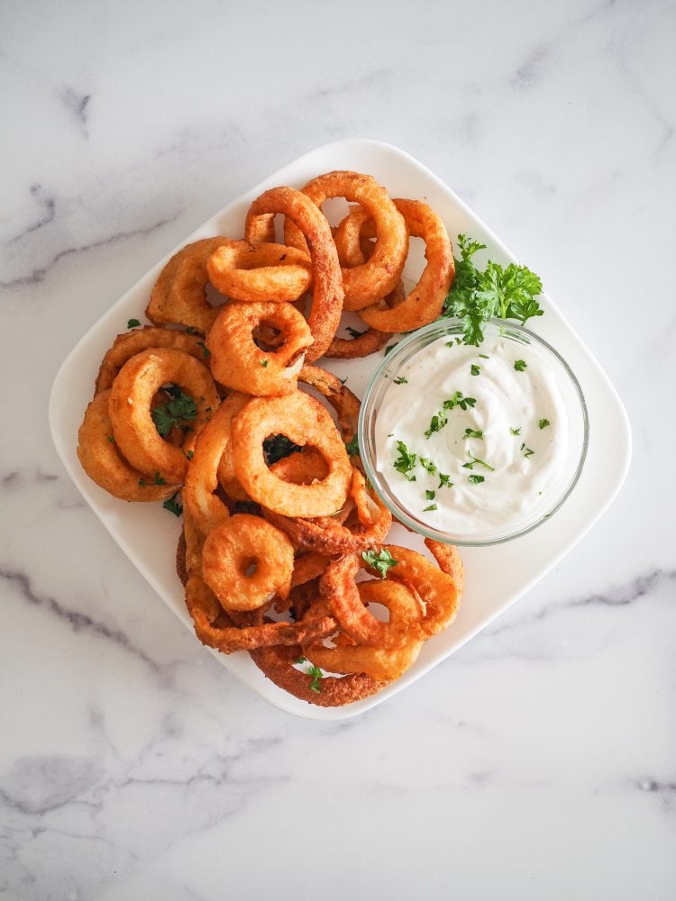 Air Fried Frozen Onion Rings - Overhead view of plate of air fried onion rings with garlic dipping sauce and parsley.