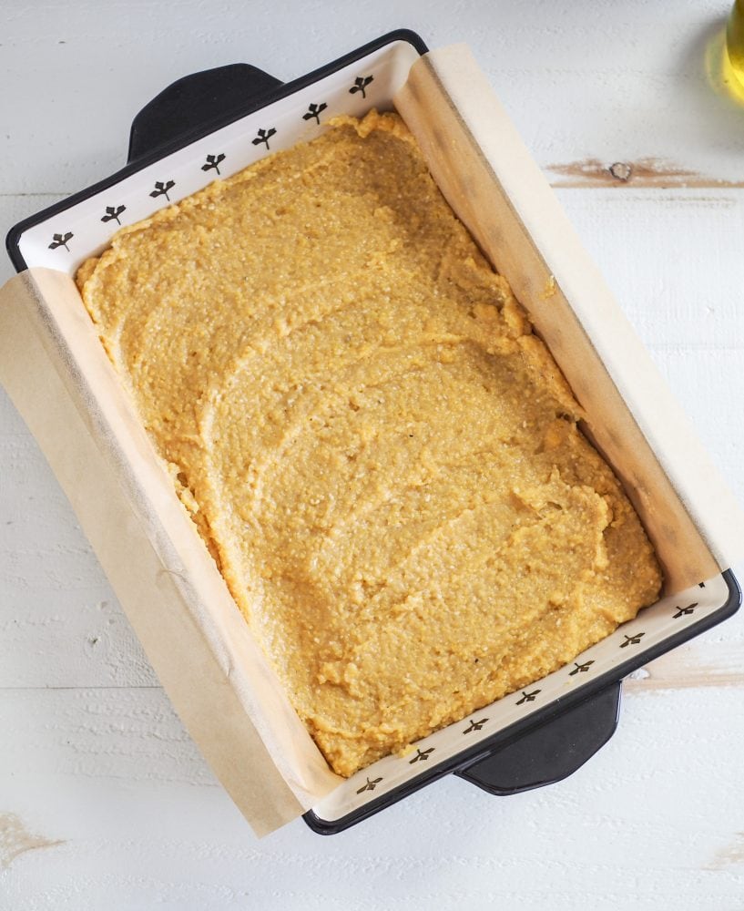 Overhead look into a ceramic 9x13" casserole dish with polenta spread onto parchment paper.