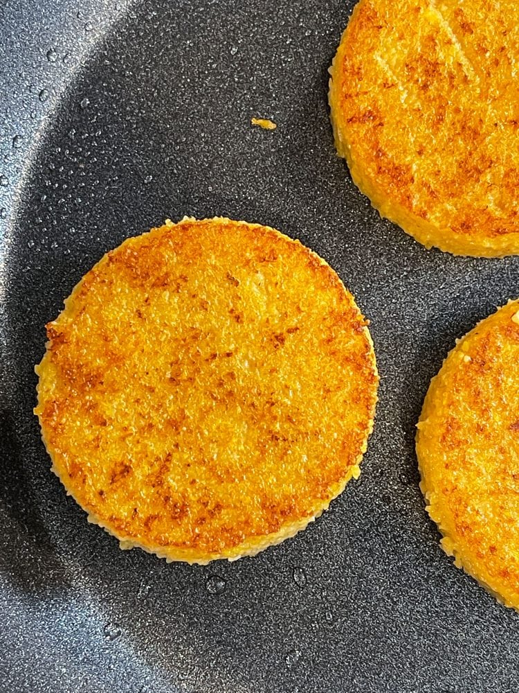 Round polenta cakes cooking in a frying pan.