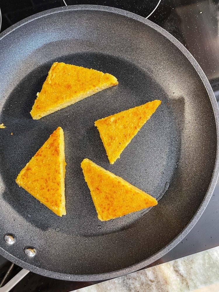 Triangular polenta cakes cooking in a frying pan.