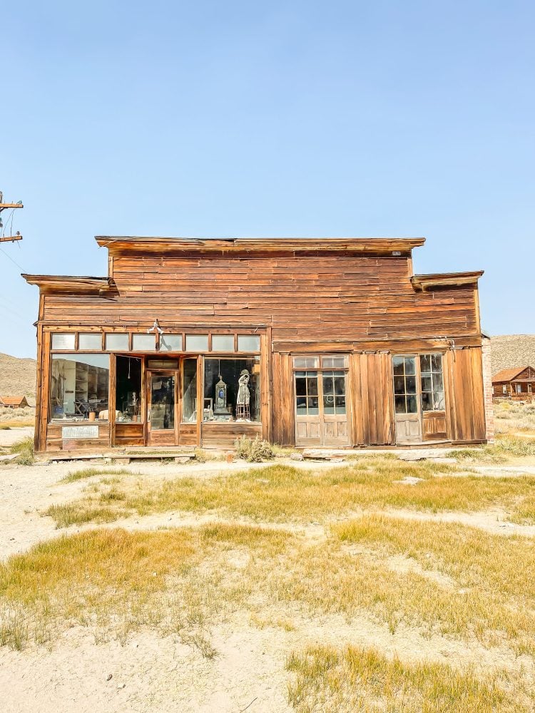 Photo of general store inside Bodie historic state park. It's made of rustic wood in arrested decay, and there is an old dress form in the window.