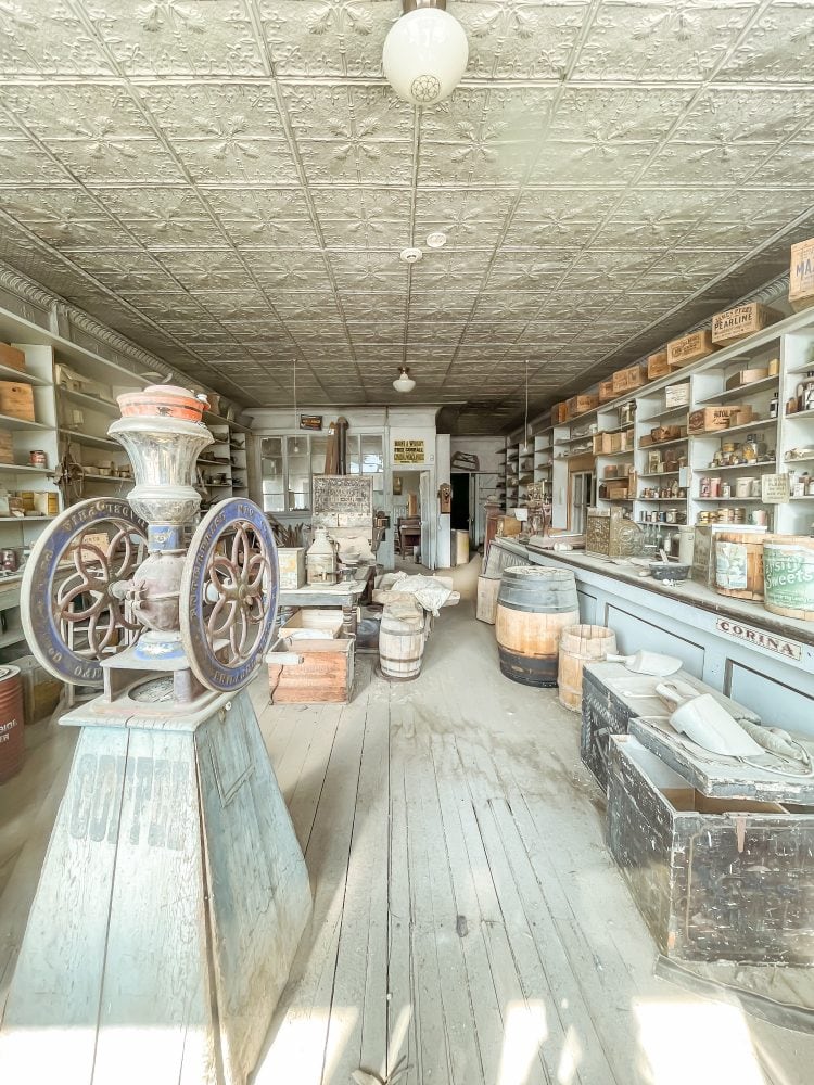 A look inside Bodie ghost town's general store with stocked shelves on both sides, wood barrels against the counter, and an old coffee display up front.