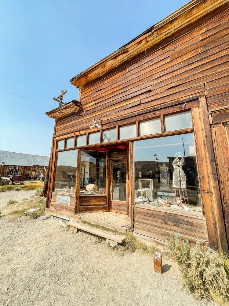 Side angle view of the entrance to Bodie's general store with large glass windows to display goods and an old dress form still in the window.