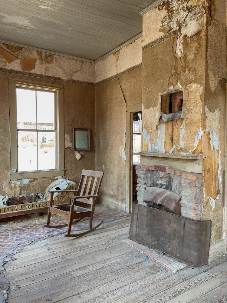 Inside the entrance to the Miller House in Bodie State Park with the fireplace and seating area, decaying chairs and peeling wallpaper.
