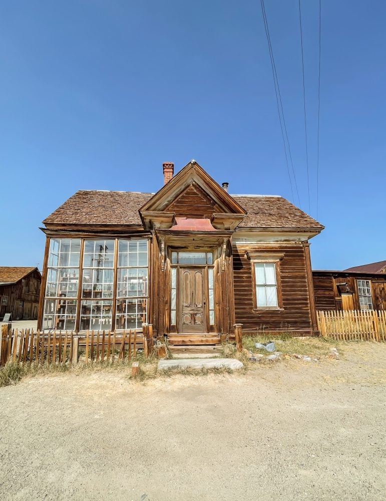 Front view of Bodie Ghost Town's apothecary with large glass windows to the right and a centered front entrance.
