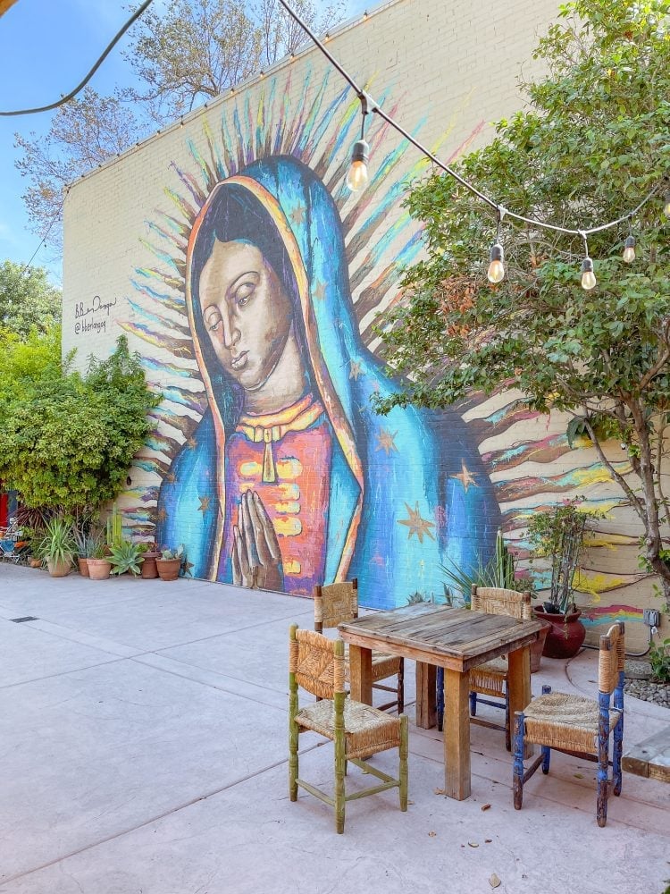 Inside the courtyard at Kulture, featuring a mural of Virgin Mary, cafe style table and chairs, and market lights.