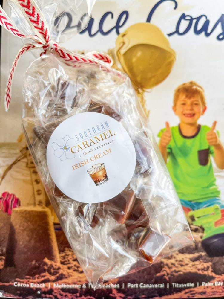 A bag of Southern Caramel, Irish Cream flavored, tied with a red and white striped ribbon and laid on a Space Coast magazine cover with little boy in green shirt giving a thumbs up.