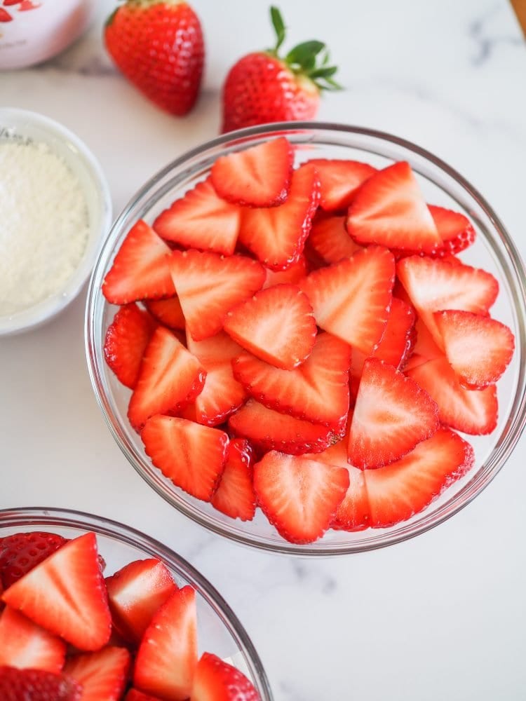 Closeup overhead shot of bright red sliced strawberries in a clear glass bowl.