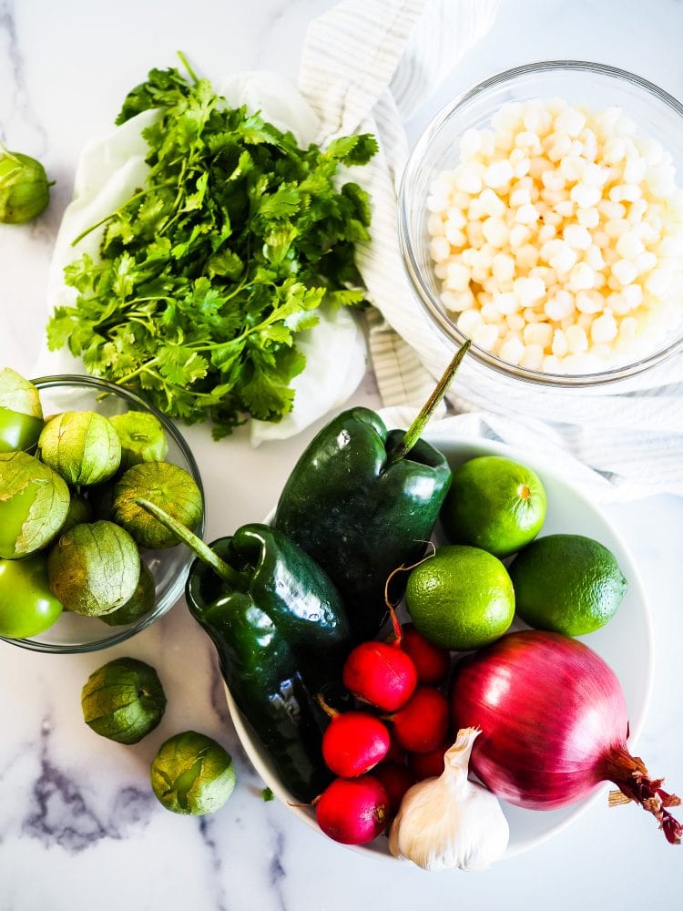 Pozole verde ingredients including cilantro, tomatillos, hominy, poblano peppers, lime, and radishes.