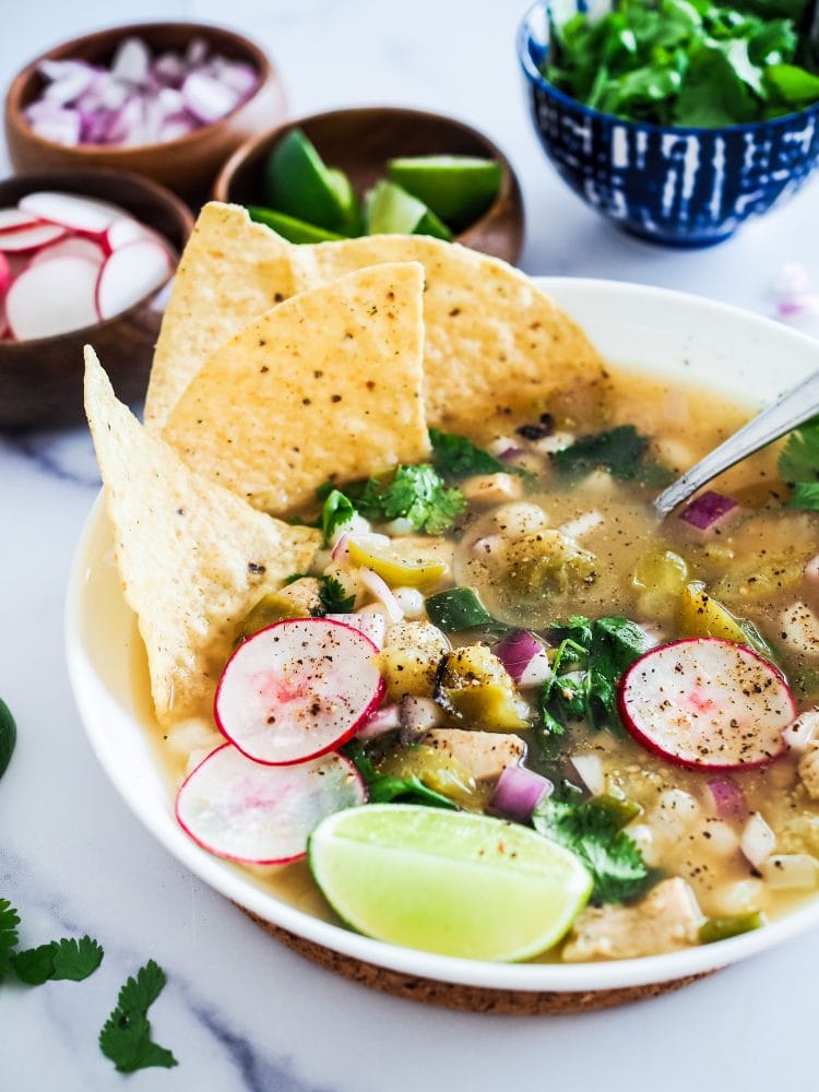bowl of pozole verde topped with lime wedge, cilantro, radishes, and tortilla chips