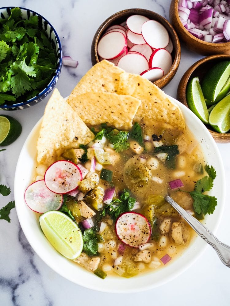 bowl of pozole verde topped with radishes, lime, cilantro, and tortilla chips.
