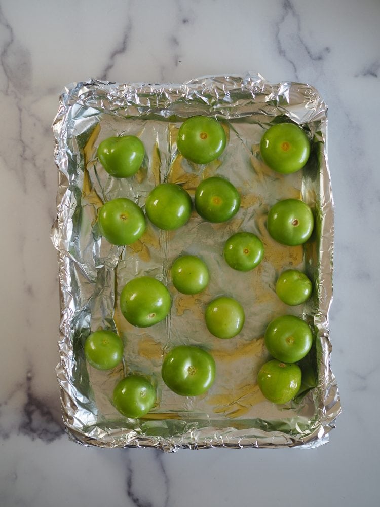 tomatillos drizzled with oil on a foil lined baking sheet