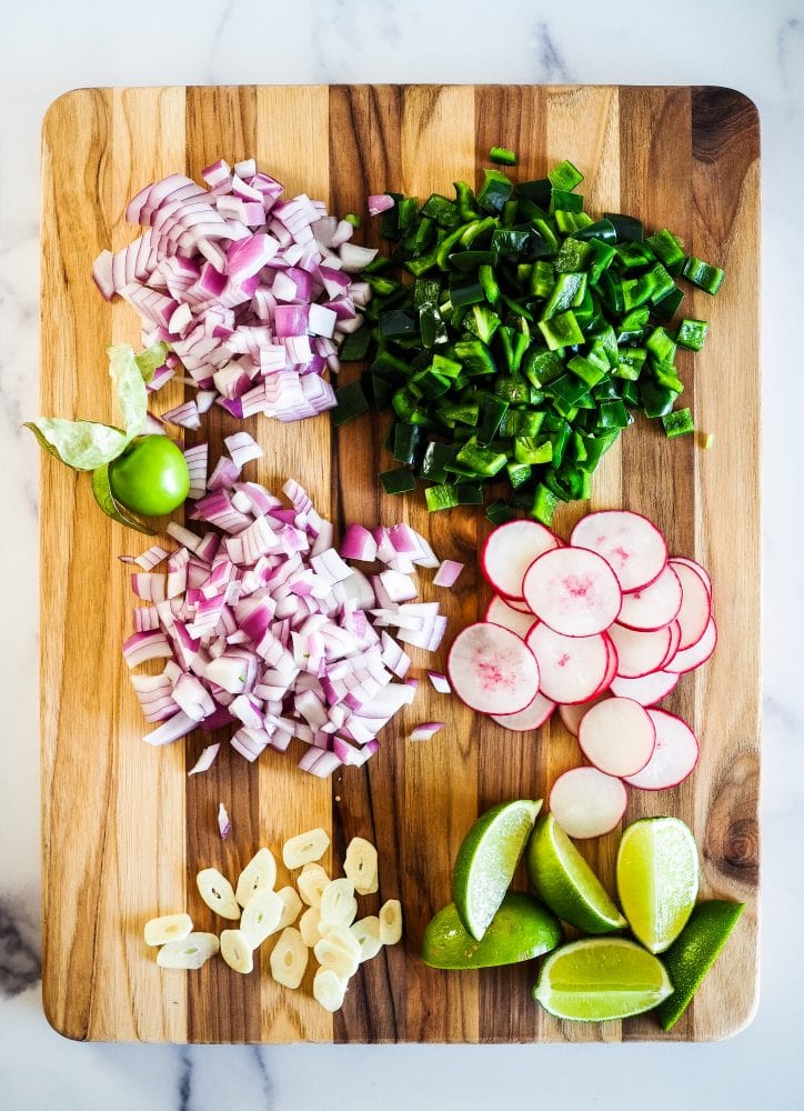 wood cutting board with diced red onion, sliced radishes, diced poblano peppers, and lime wedges