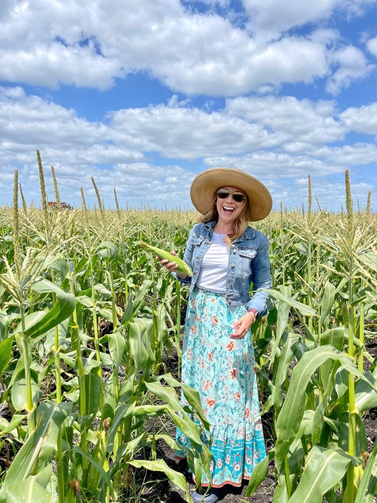 Rachelle standing in a corn field holding an ear of corn.